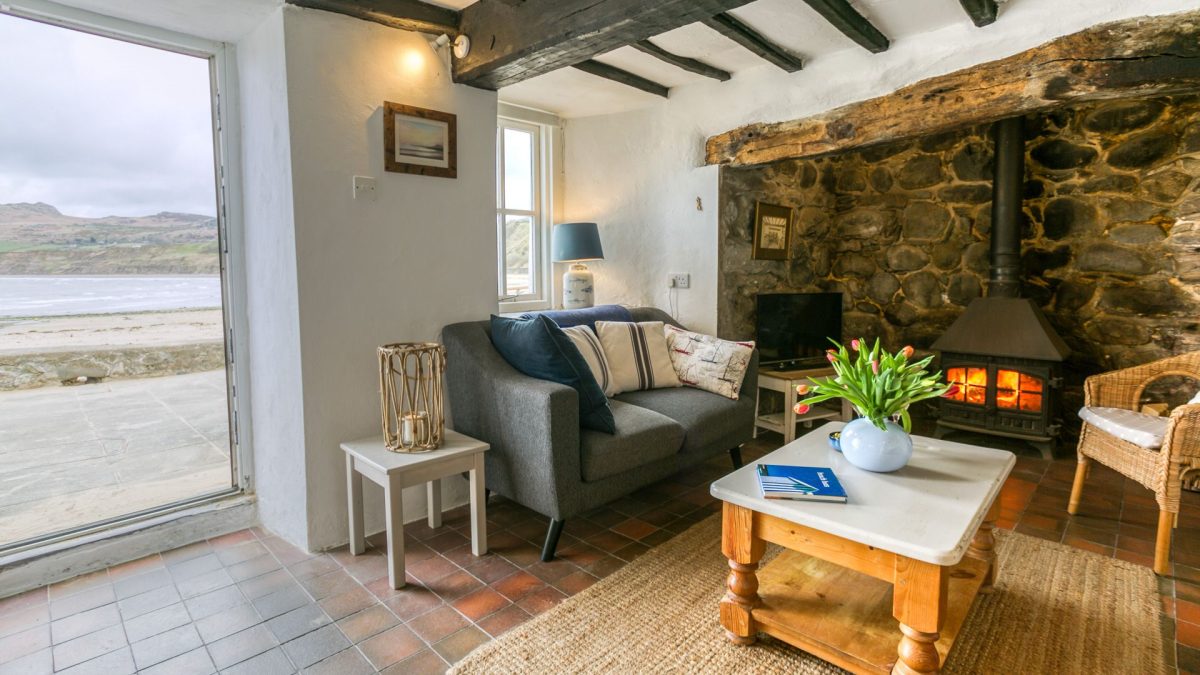 Hen Dafarn living room with a log burner, sofa, arm chair and views out to the sea.